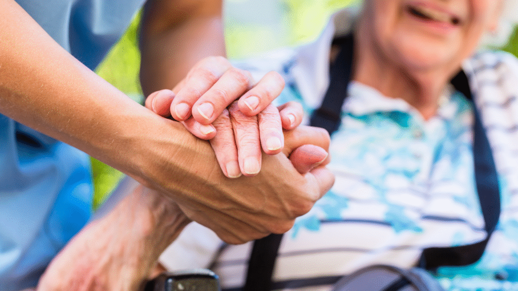 A carer gently holding an older person’s hand during a wellness check in Christchurch, New Zealand