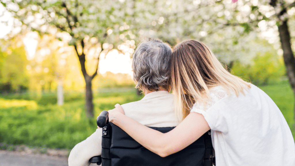 A younger person comforting an older adult in a wheelchair outdoors in Christchurch, New Zealand