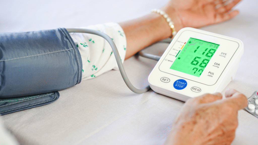 Close-up of an older person’s hand beside a digital blood pressure monitor during a wellness check at home in Christchurch and Tauranga